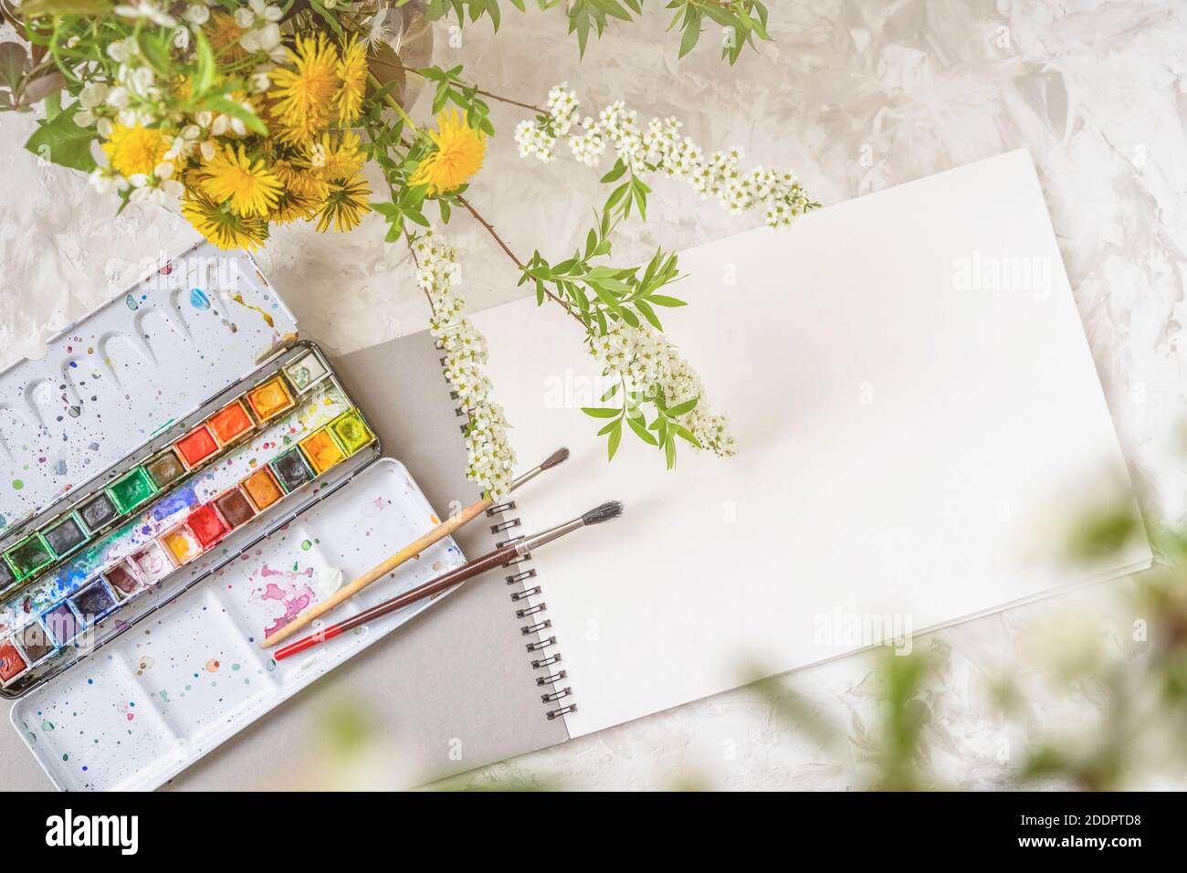 Vue de dessus d'une table avec un carnet d'esquisses ouvert, des peintures et des pinceaux à côté d'un bouquet de fleurs printanières, espace de copie. Passe-temps Banque D'Images