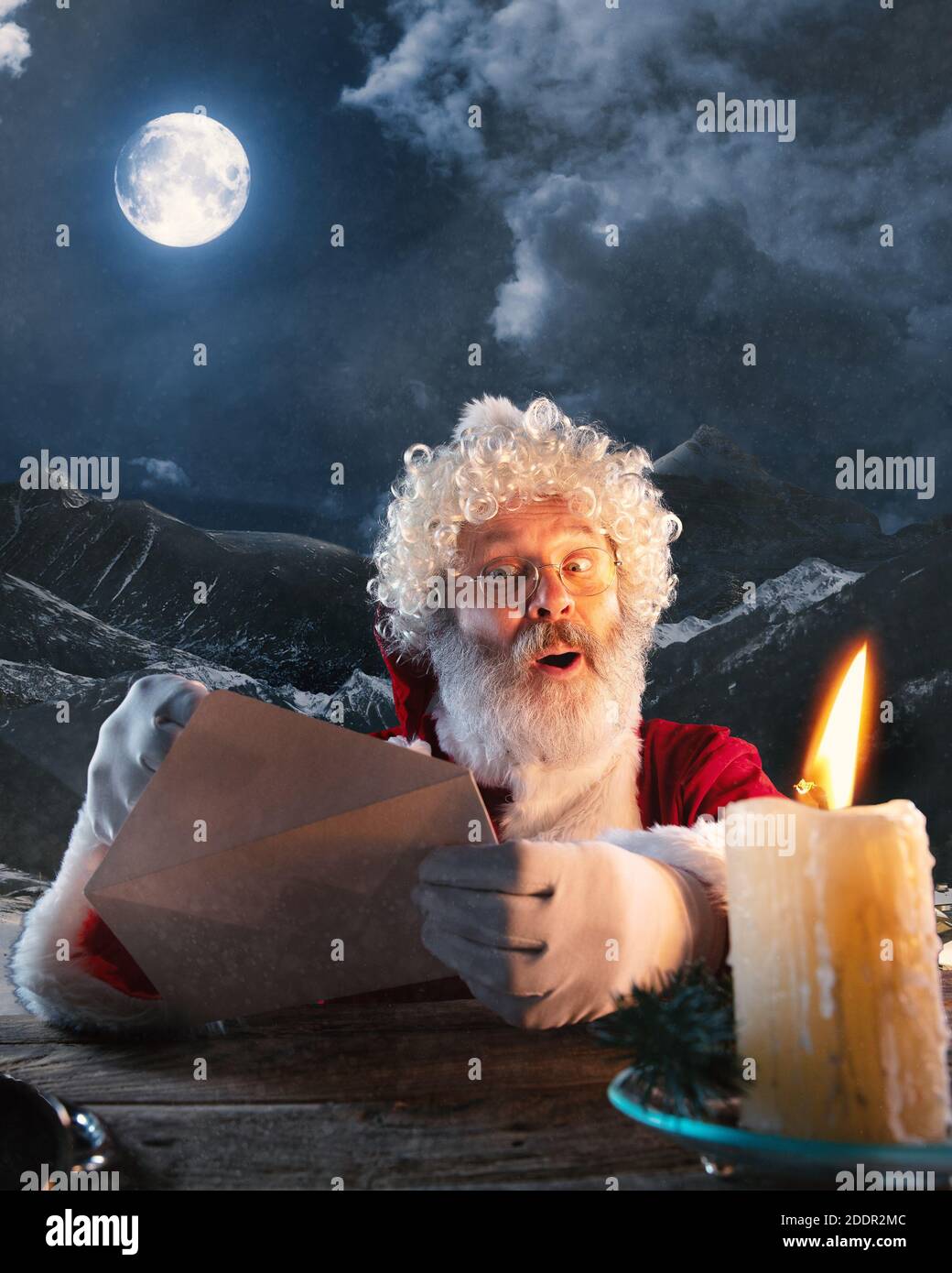 Cordialement. Le Père Noël émotionnel félicite le nouvel an 2021 et Noël. Homme en costume traditionnel envoyer une lettre, liste de souhaits illuminée avec bougie et forêt de nuit sur fond. Hiver, vacances Banque D'Images