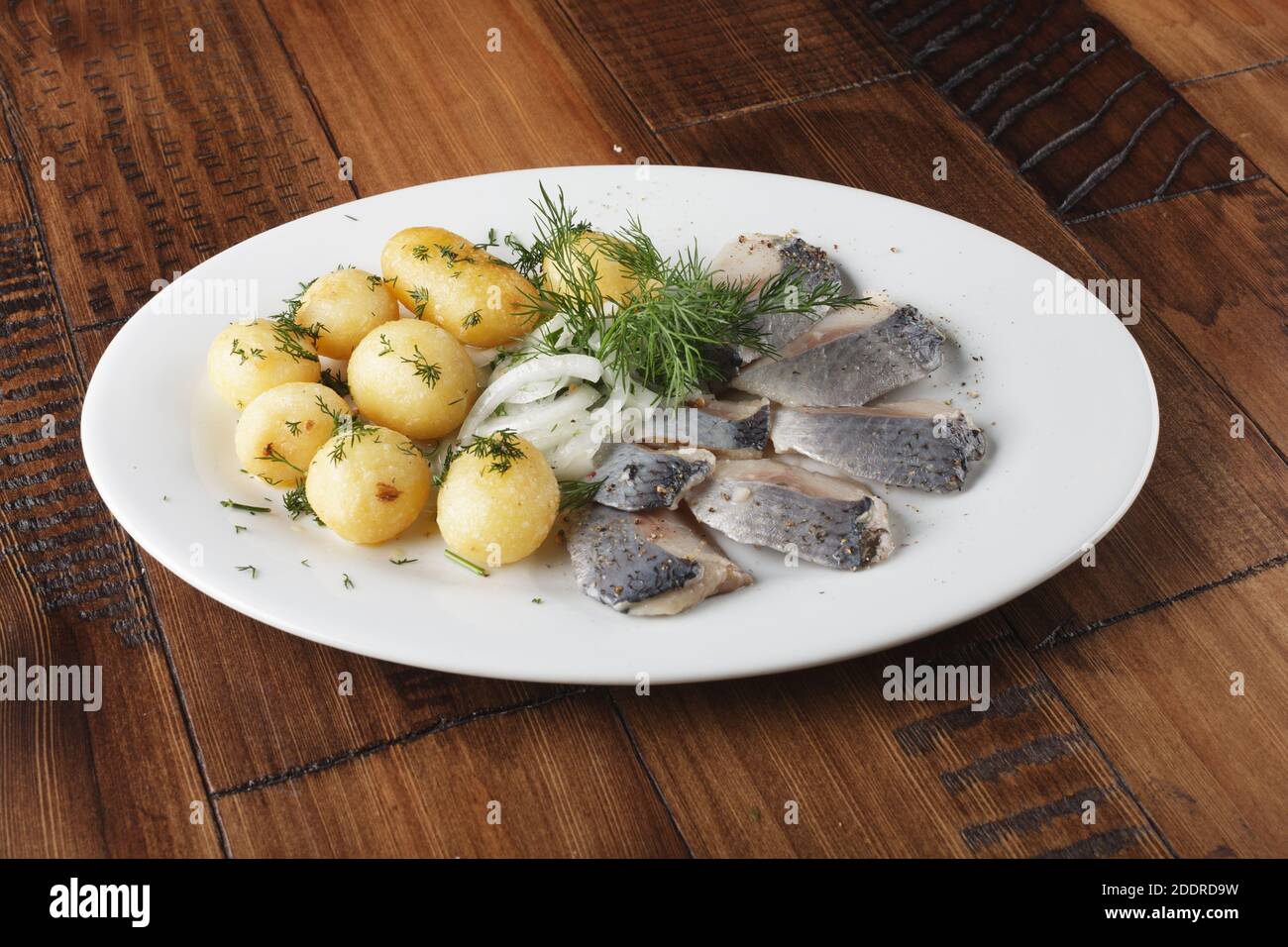 Poisson de hareng avec de jeunes boules de pommes de terre sur une assiette blanche. fond en bois. Banque D'Images