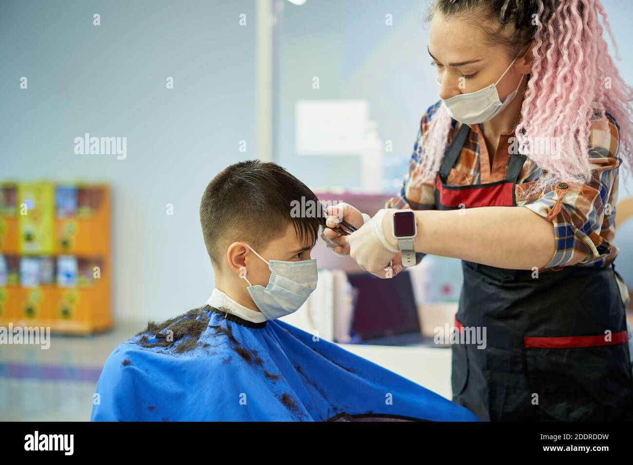 Adolescent dans le masque facial faisant la coupe de cheveux au magasin de coiffure Banque D'Images