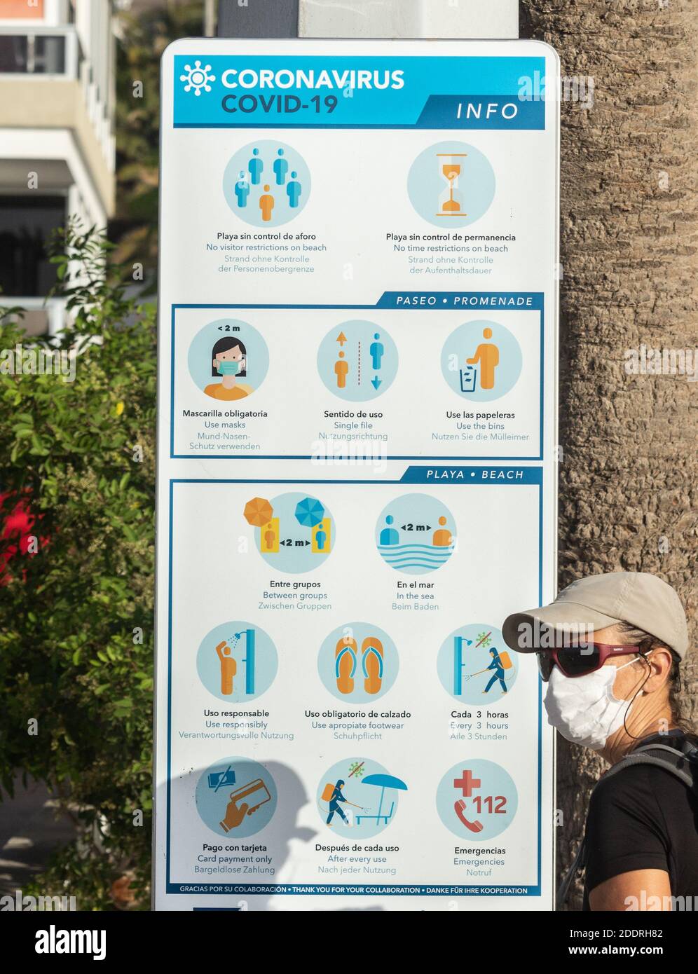 Femme portant un masque facial/couvrant lisant les règles du coronavirus sur la plage à l'intérieur Espagne Banque D'Images