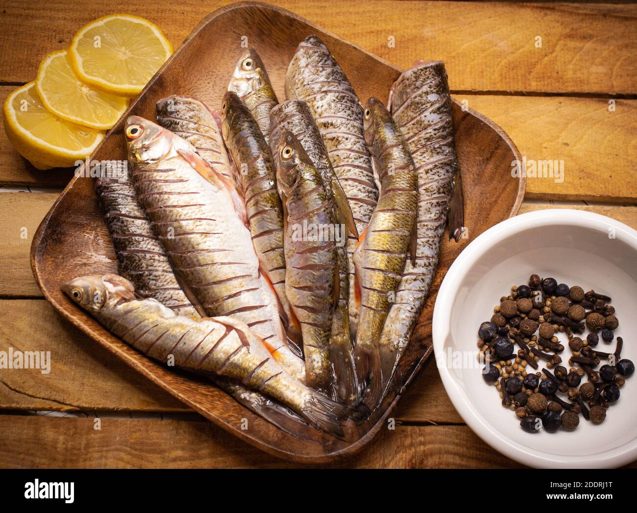 Vue de dessus chub de poisson frais sur un carré de bois brun assiette sur fond de bois décorée de citron et d'épices dans la tasse blanche Banque D'Images