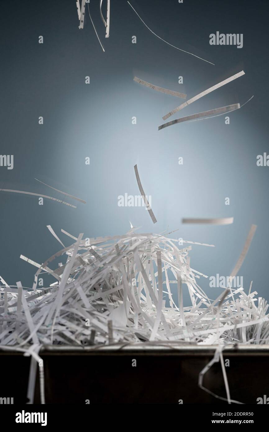 Une pile de bandes de papier déchiquetées se trouve dans une boîte en métal et, par le dessus, d'autres bandes tombent avec le flou de mouvement. Banque D'Images