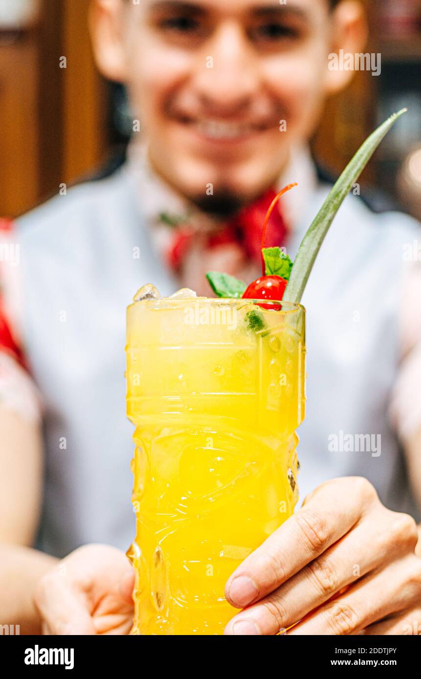 Barman montrant un cocktail dans un verre de tiki sur un bar compteur sur un fond flou de bouteilles dans une barre Banque D'Images