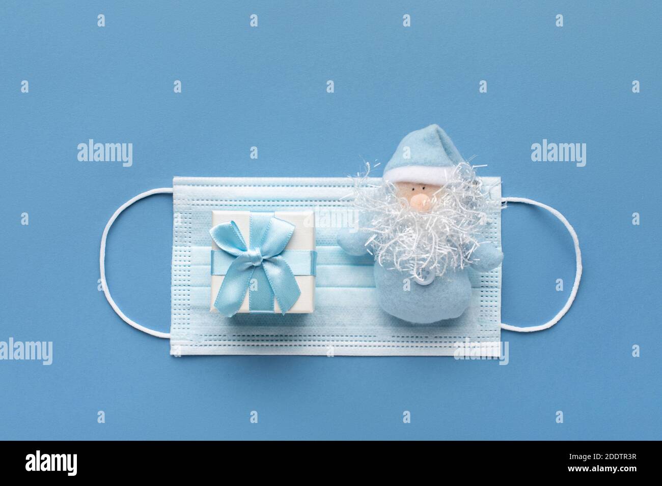 Carte postale avec félicitations pour le nouvel an et noël. Plat en masque, boîte cadeau et bonhomme de neige bleu pastel. Concept de nouvelle normalité A. Banque D'Images