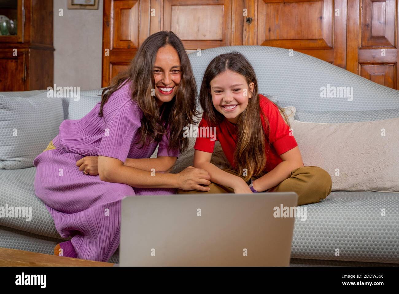 Maman souriante et petite fille drôle sont assis sur le canapé tenir portable vague chat vidéo parler sur la webcam - heureux avant-chooler fille enfant et mère Banque D'Images