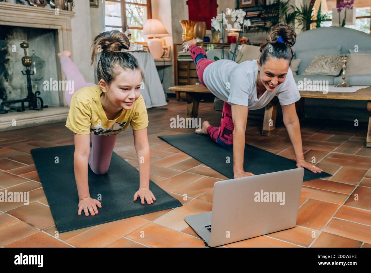 Mère et fille pratiquant des cours de yoga en ligne à la maison pendant la quarantaine pendant la pandémie du coronavirus. Famille faisant du sport ensemble en ligne Banque D'Images