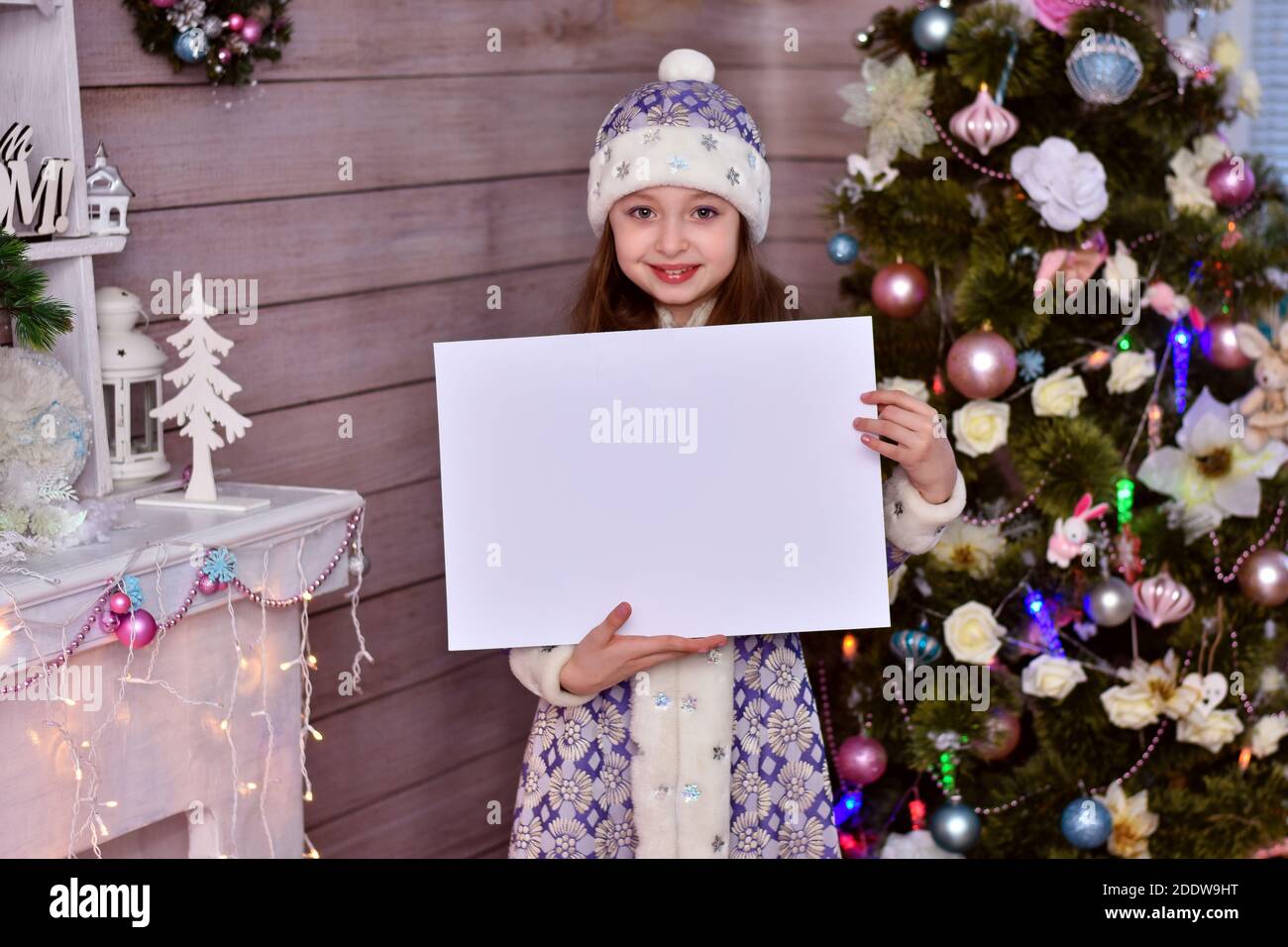 Une fille dans un costume d'aide du Père Noël. La fille tenant un morceau de papier vierge et pointant vers l'espace de copie. Banque D'Images