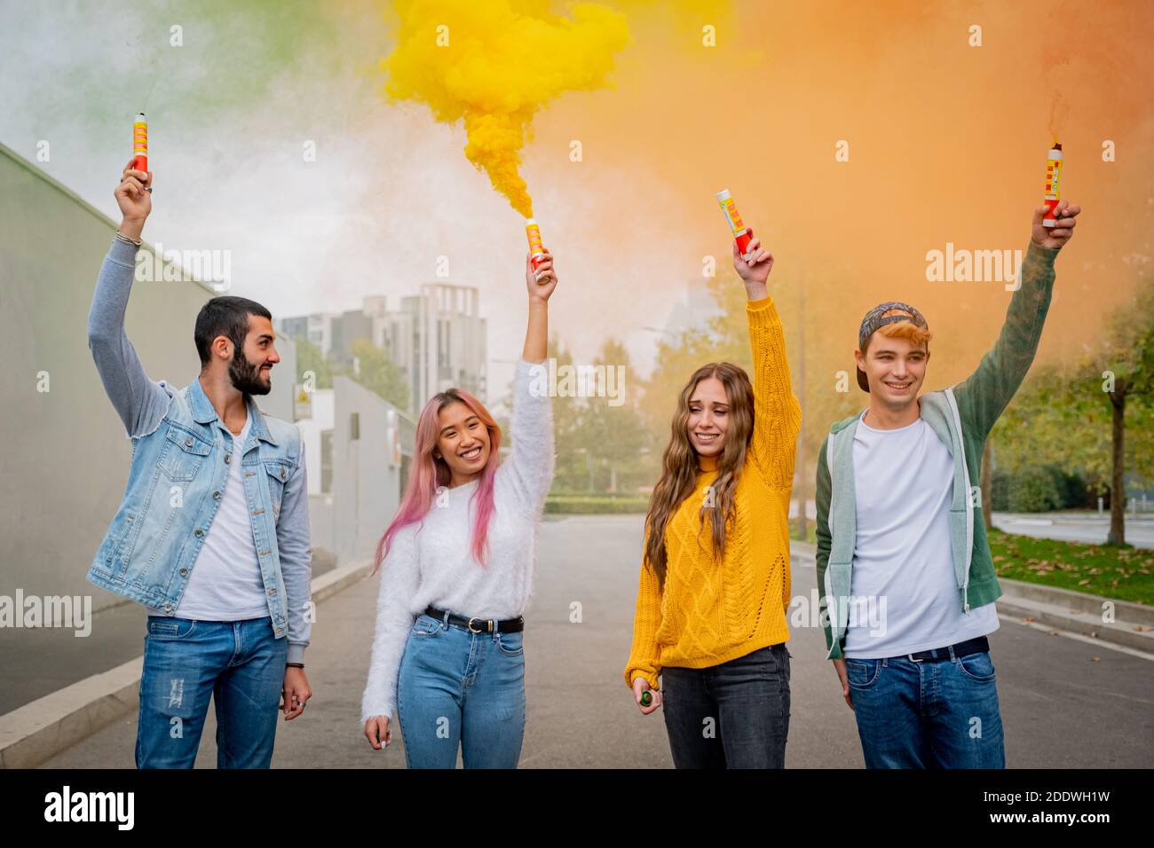 De beaux jeunes gens se tiennent dans la rue et tiennent la lumière de couleur Bombes de fumée - des amis heureux s'amuser dans la rue avec des bombes de fumée multicolores Banque D'Images