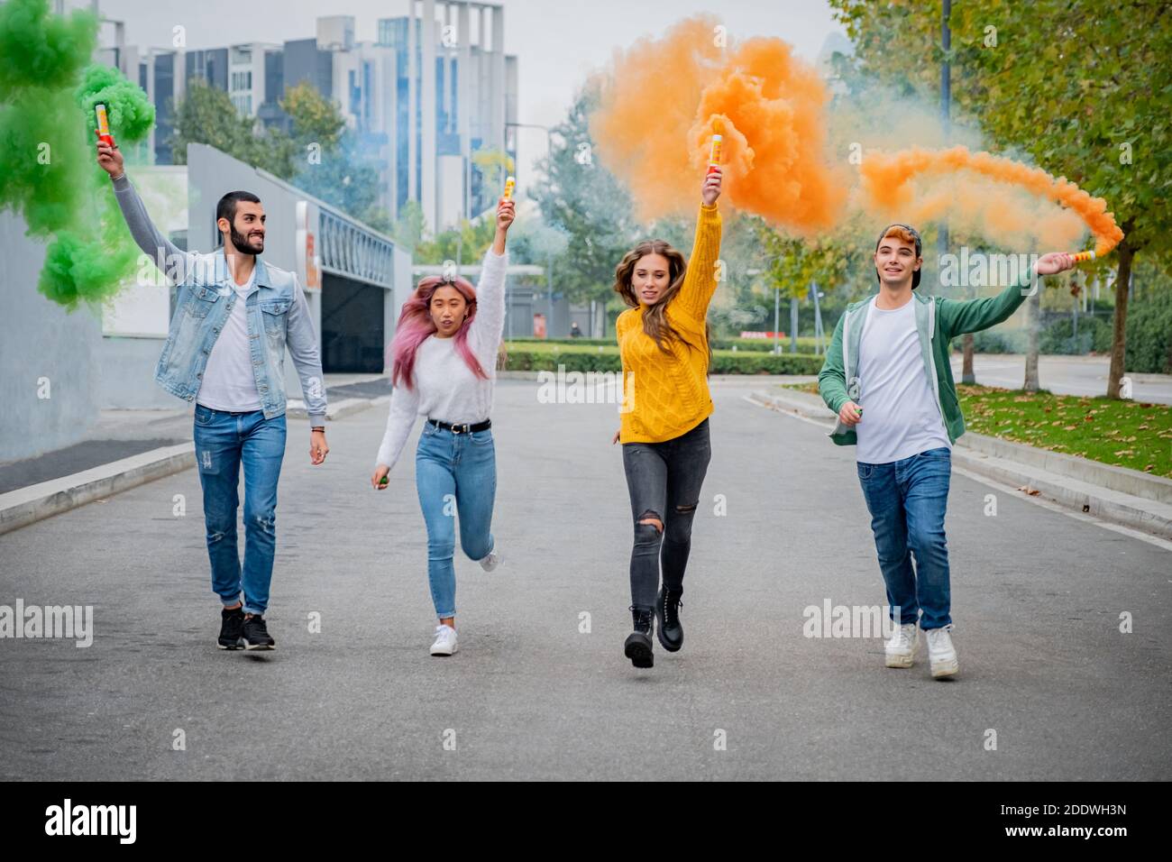 De beaux jeunes gens se tiennent dans la rue et tiennent la lumière de couleur Bombes de fumée - des amis heureux s'amuser dans la rue avec des bombes de fumée multicolores Banque D'Images
