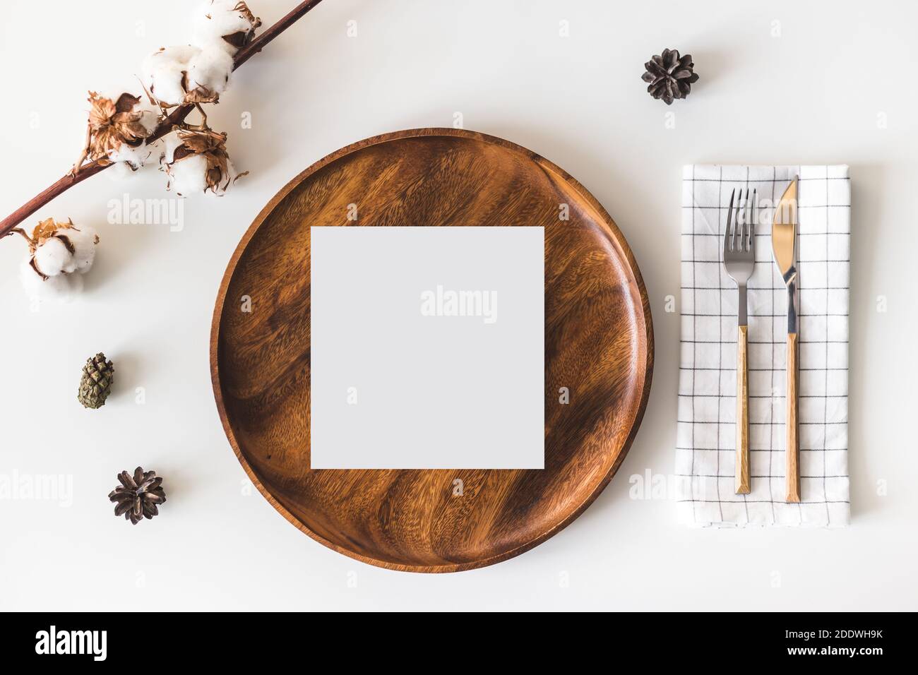 Carte de vœux en papier vierge sur plat en bois, couverts avec serviette à carreaux, fleurs en coton. Arrière-plan de table blanc. Flat lay, vue de dessus Banque D'Images
