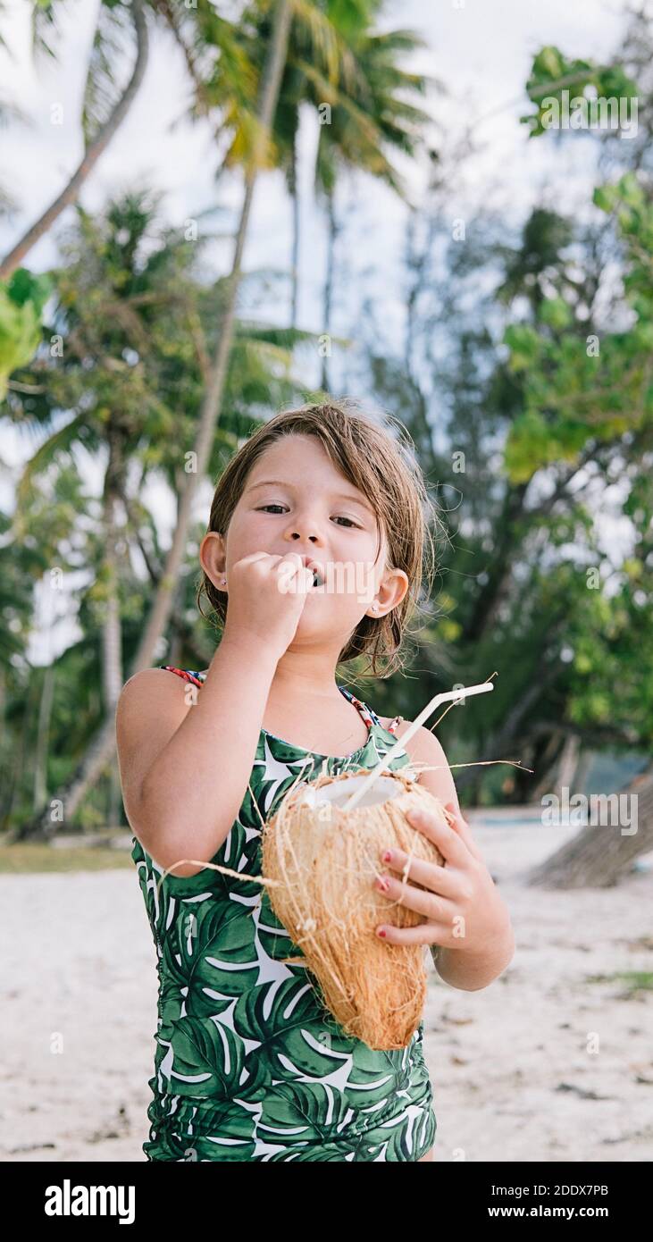 Photo de stock de petite fille appréciant la journée à la plage et tenant une noix de coco. Banque D'Images