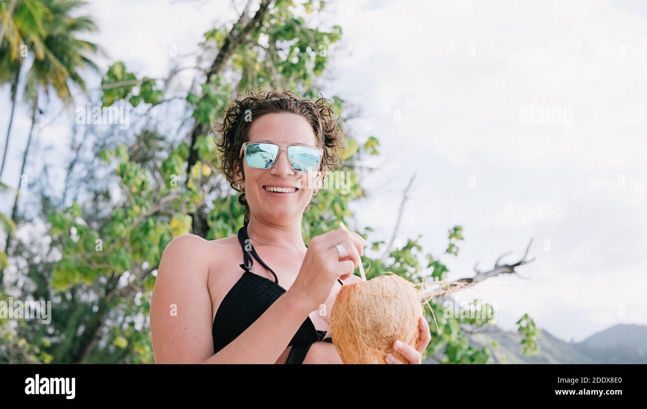 Photo de la femme gaie qui profite de la journée à la plage et tient une noix de coco. Banque D'Images