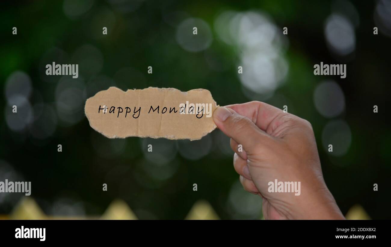 Happy Monday texte sur les mains tenant du papier déchiré avec un arrière-plan sombre flou. Devis du lundi Banque D'Images