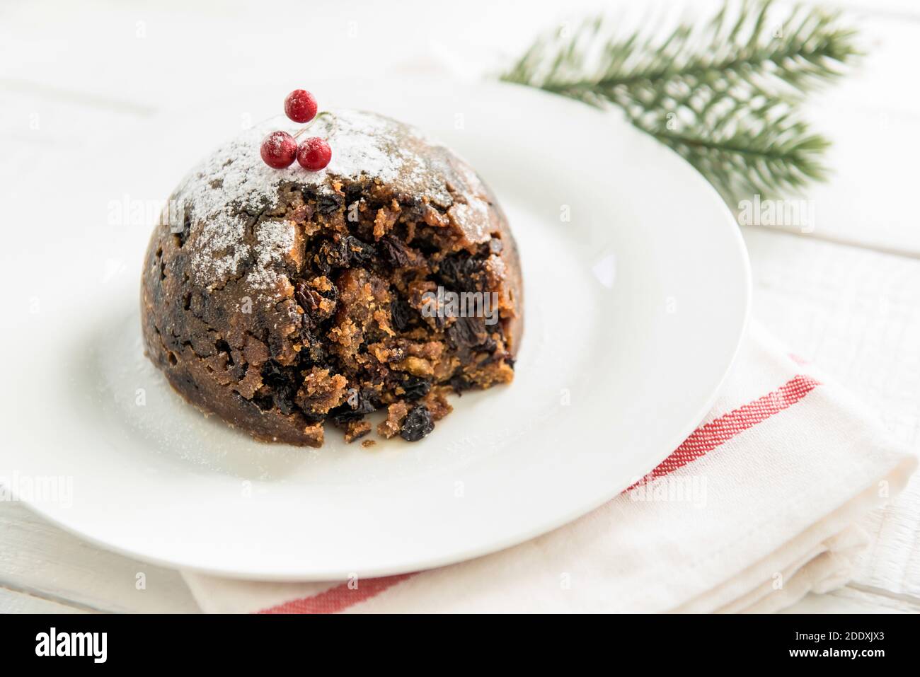 Pouding traditionnel de Noël ou de prune recouvert de sucre glace en poudre et baies rouges sur plaque blanche Banque D'Images