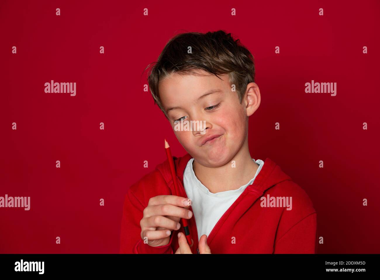 un jeune garçon d'école cool pose avec un crayon rouge avant d'arrière-plan rouge Banque D'Images