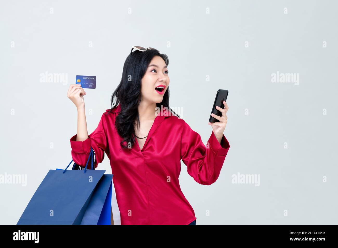 Surpris jeune femme asiatique magasiner en ligne avec un smartphone et payer par carte de crédit sur fond gris studio Banque D'Images