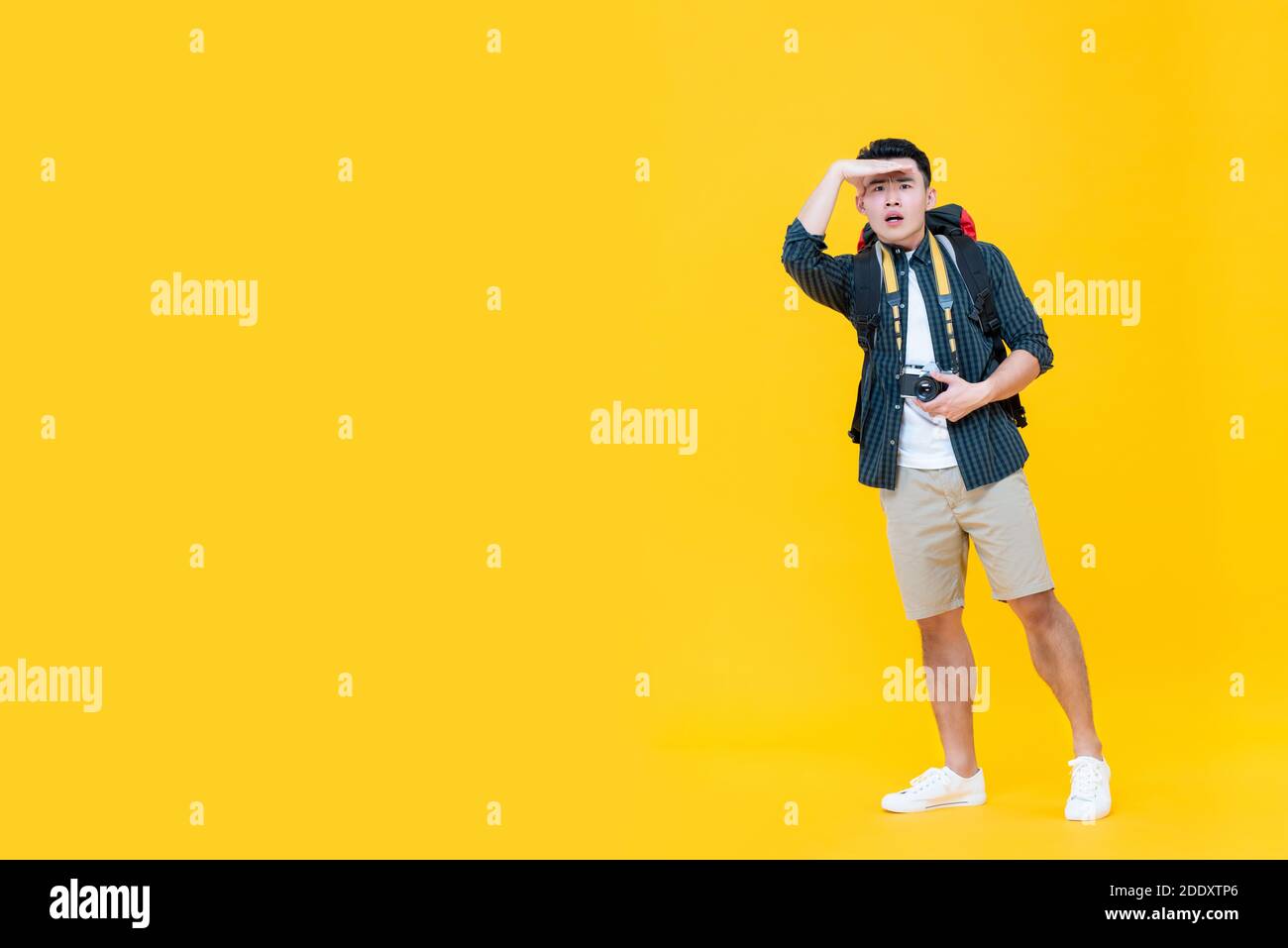 Homme touristique asiatique regardant loin avec la main sur le front isolé sur fond jaune avec espace de copie Banque D'Images