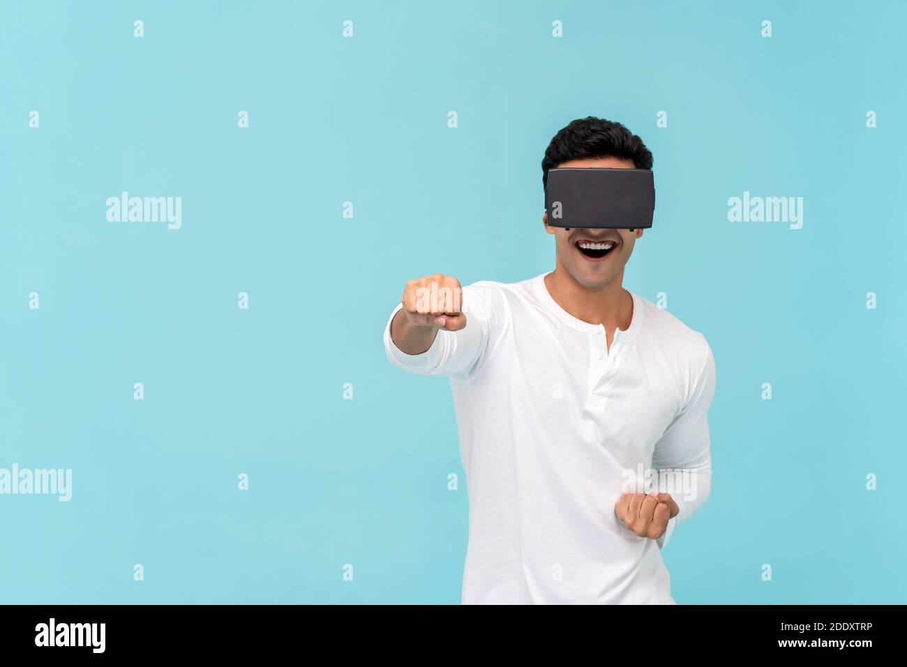 Homme asiatique excité portant des lunettes de réalité virtuelle ou VR et Poinçonner tout en jouant à un jeu vidéo de simulation 3D sur bleu clair arrière-plan avec espace de copie Banque D'Images