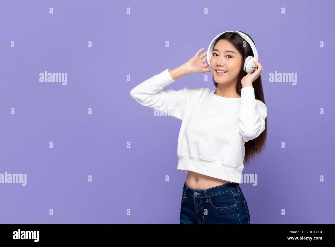 Jeune femme asiatique mignonne en souriant et en touchant des écouteurs ecouter de la musique et danser isolés sur fond violet Banque D'Images