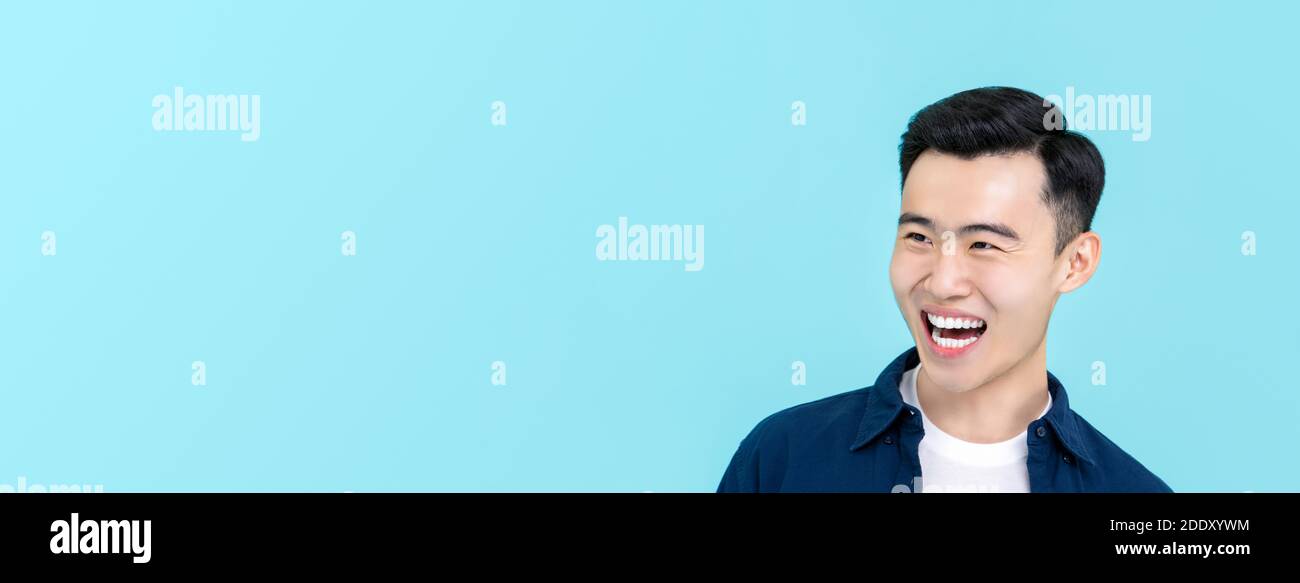 Beau et heureux jeune homme asiatique souriant et regardant de côté à espace de copie isolé sur l'arrière-plan de la bannière bleu clair Banque D'Images