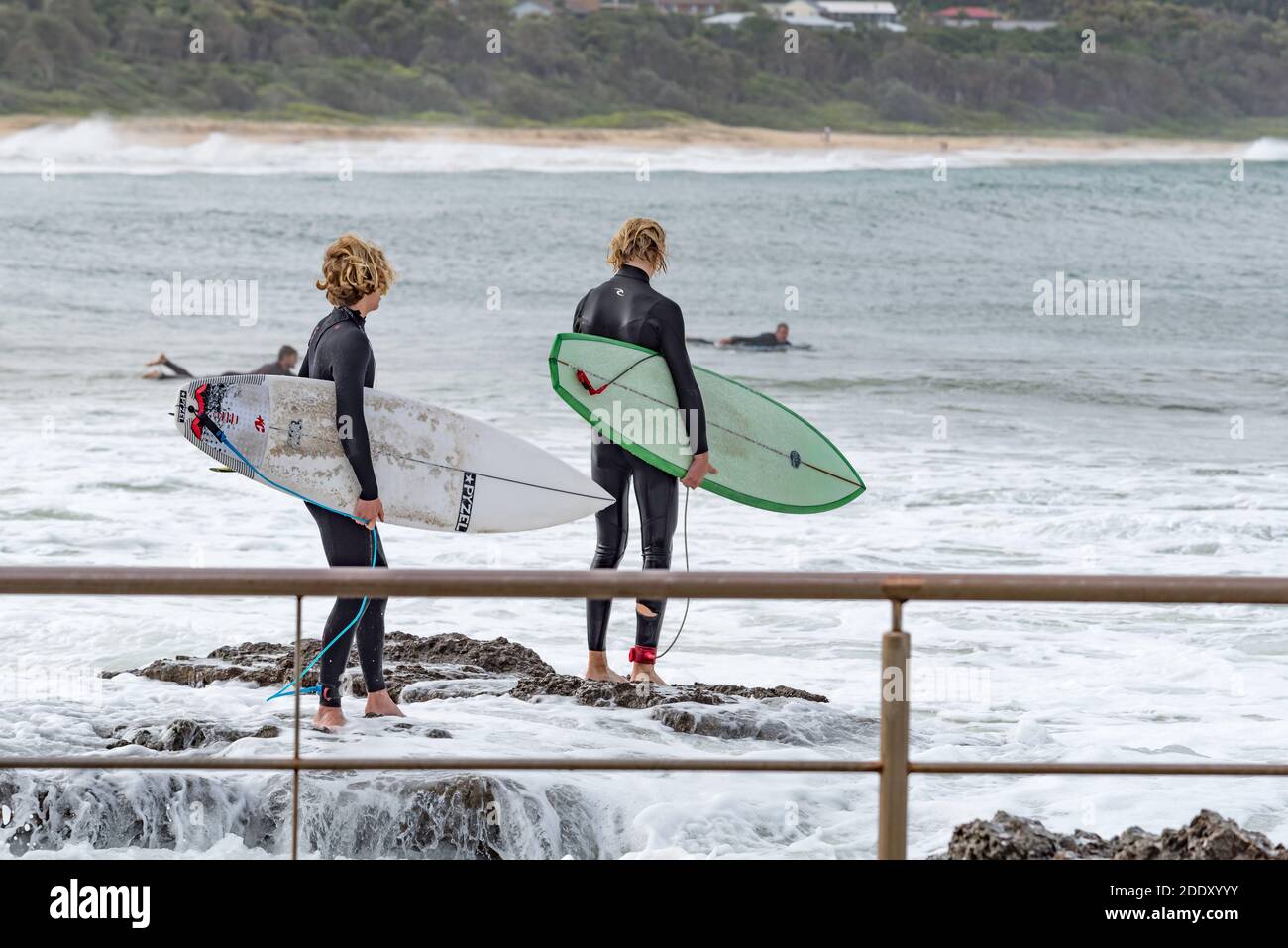 Deux jeunes cavaliers de planche de surf de sexe masculin regardent attentivement pendant qu'ils se préparent Pour sauter dans l'eau des rochers près de Black Head Beach Ocean pool en Australie Banque D'Images