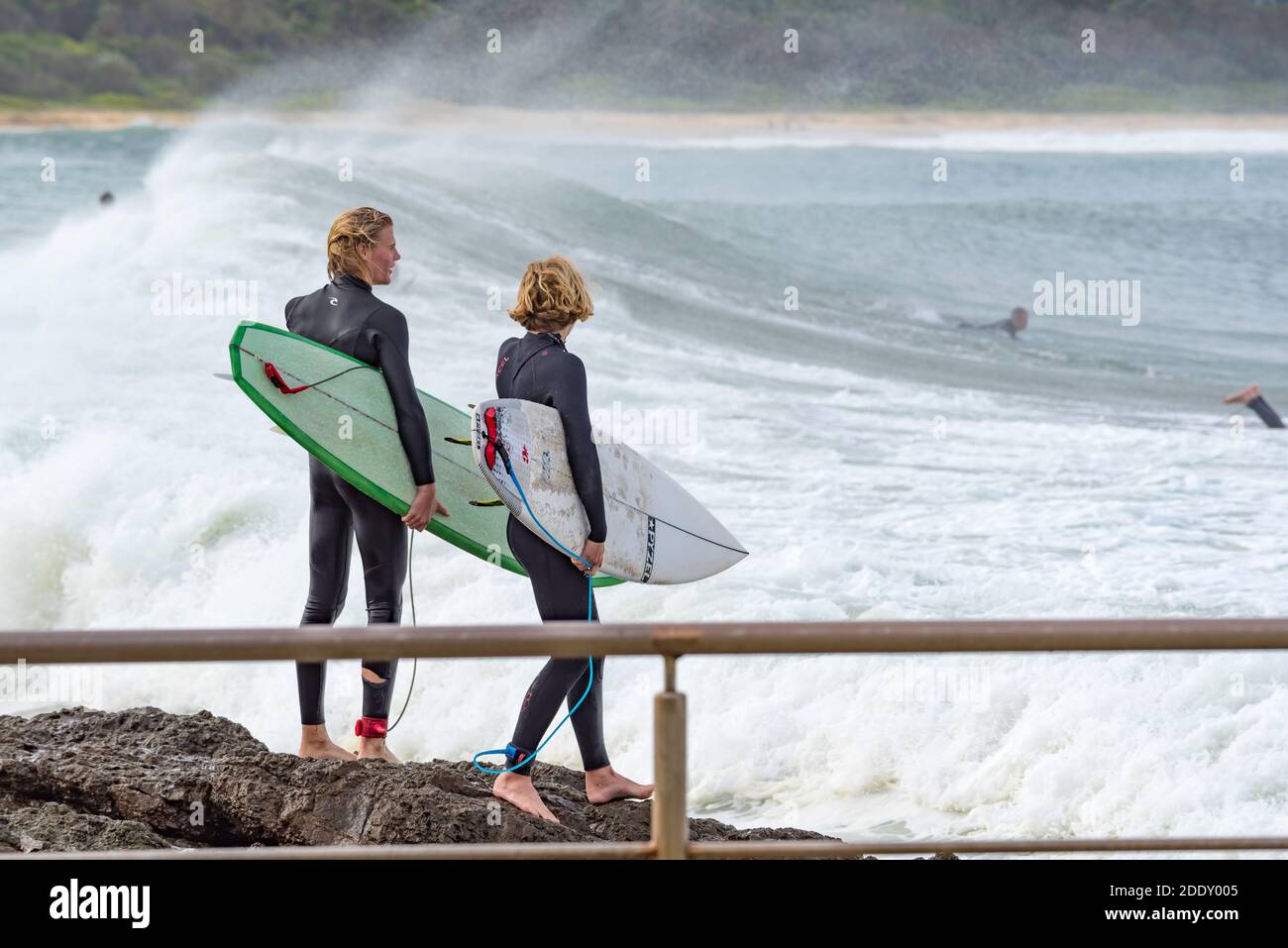 Deux jeunes cavaliers de planche de surf de sexe masculin regardent attentivement pendant qu'ils se préparent Pour sauter dans l'eau des rochers près de Black Head Beach Ocean pool en Australie Banque D'Images