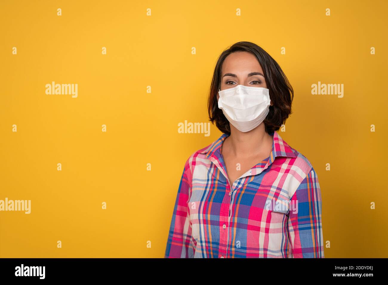 Jolie jeune femme portant un masque de protection blanc isolé sur fond jaune. Sécurité pendant une pandémie, une épidémie, une grippe saisonnière. Concept de quarantaine Banque D'Images