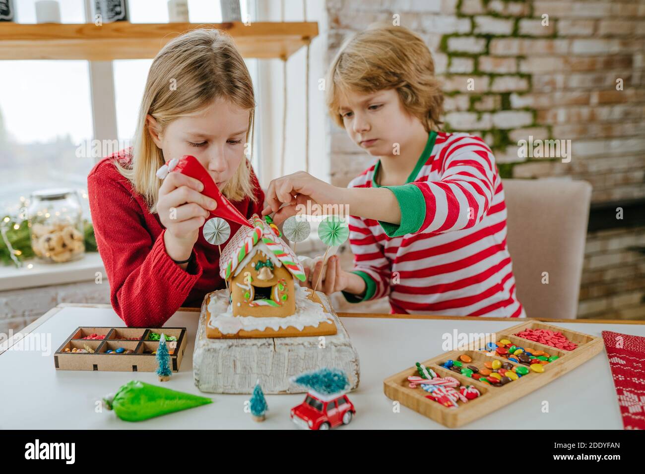 Les enfants ont décoré la maison de pain d'épice de Noël avec glaçant coloré et bonbons sur la table dans la cuisine. Noël famille maison activités concep Banque D'Images