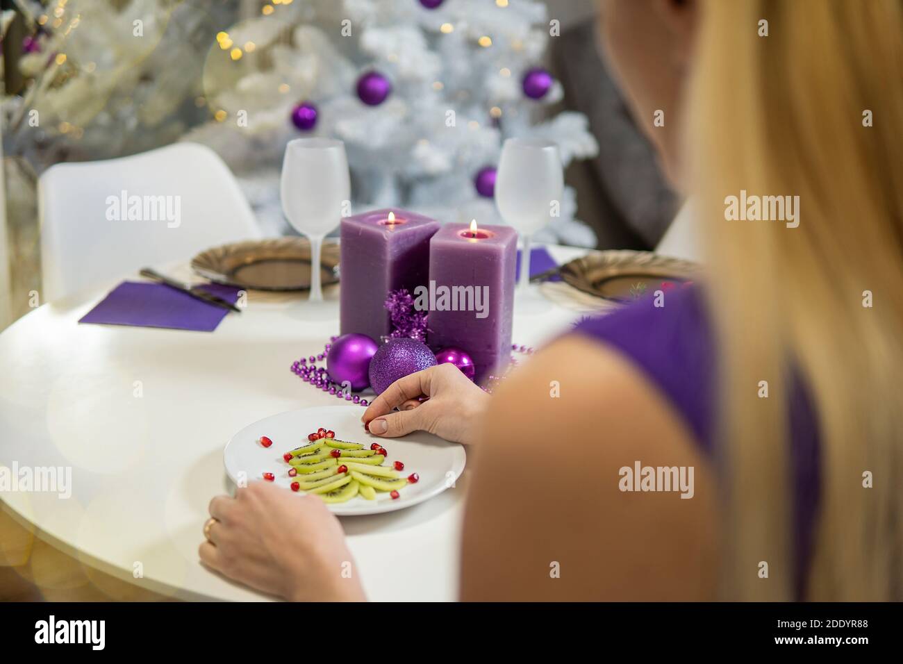 Fille fait la décoration de table de Noël. Kiwi et grenade en forme d'un arbre de noël sur un plateau et des bougies pourpres. De haute qualité Banque D'Images