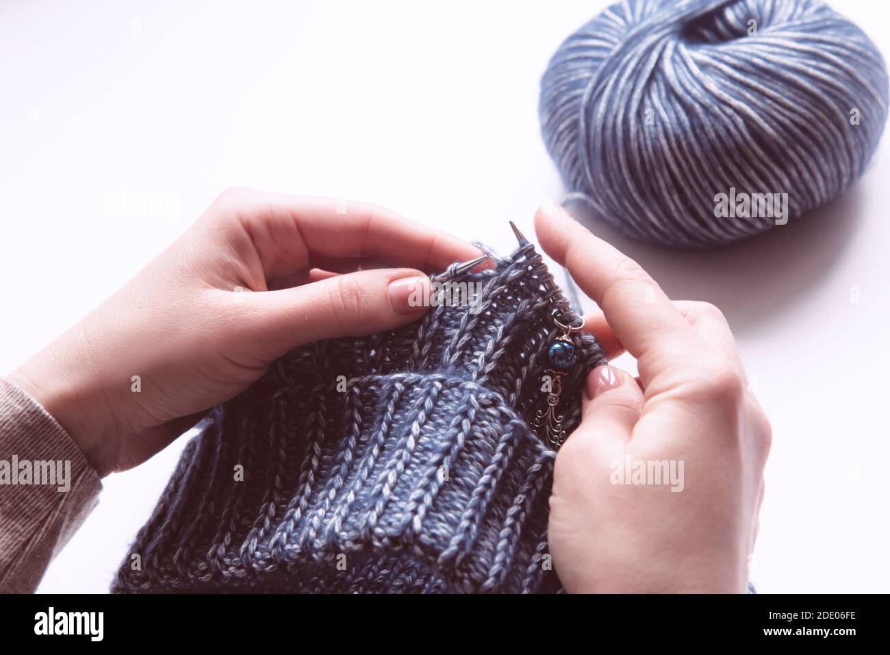 Des mains de femmes avec des aiguilles tricotées pour tricoter le chandail violet de laine sur fond blanc. Femme tricotage de vêtements en laine. Vue aérienne. Revenus de l'artisanat Banque D'Images