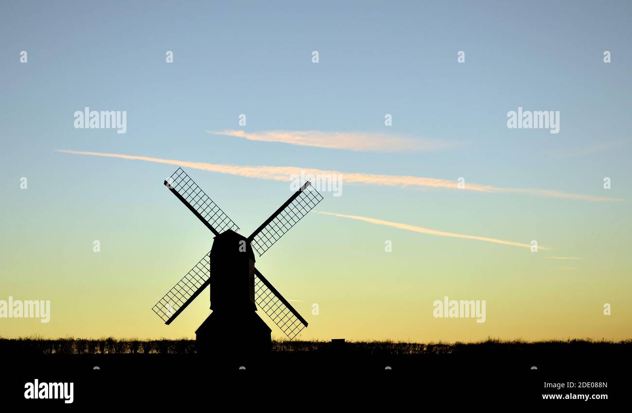 Silhouette du moulin à vent à l'horizon avec des nuages plus sombres, un ciel bleu et un horizon jaune à la lumière du soleil. Banque D'Images