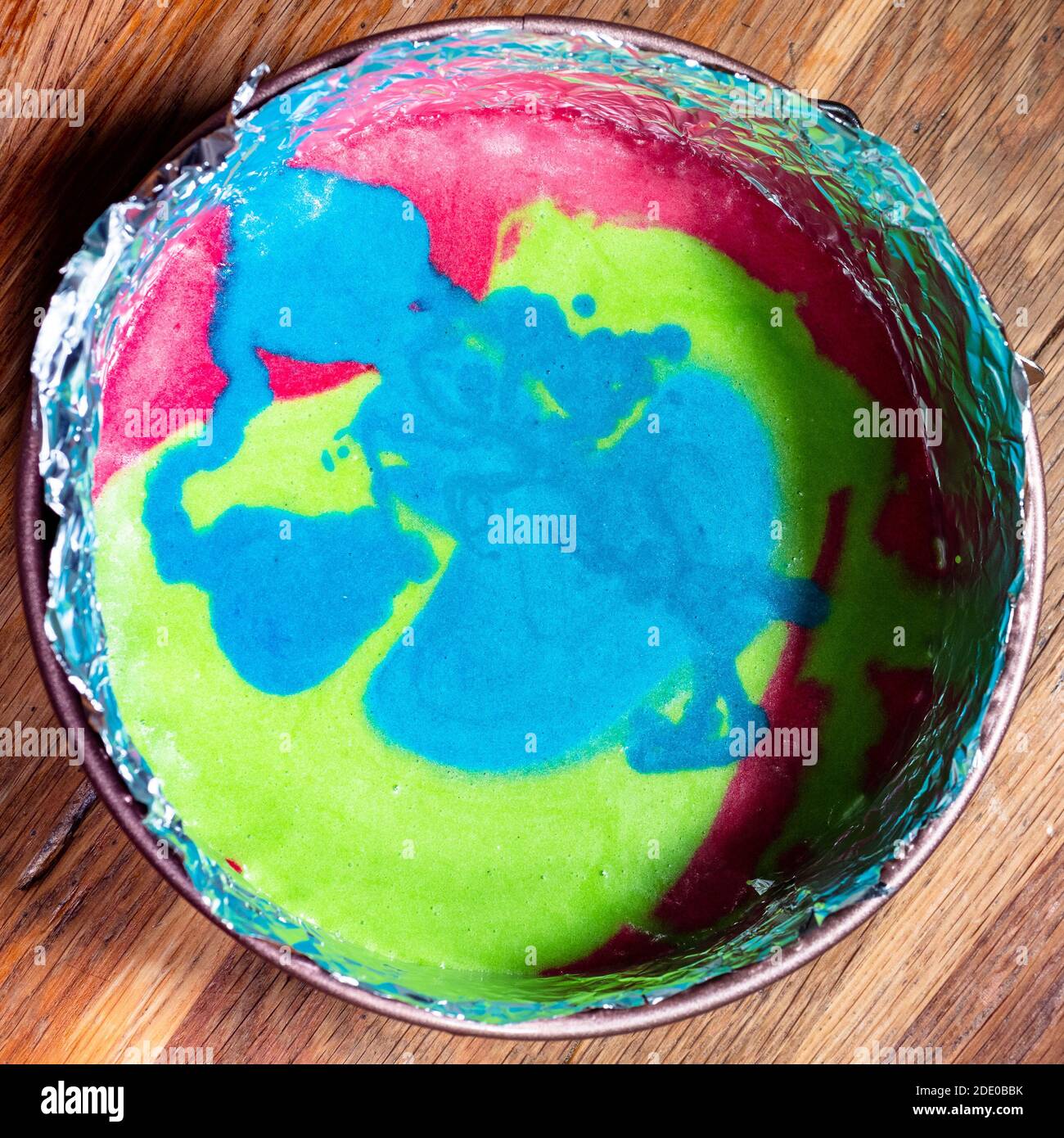 cuisiner un gâteau sucré à la maison - vue de dessus mélange multicolore de pâte crue dans un moule à charnière sur le vieux table en bois dans la cuisine Banque D'Images