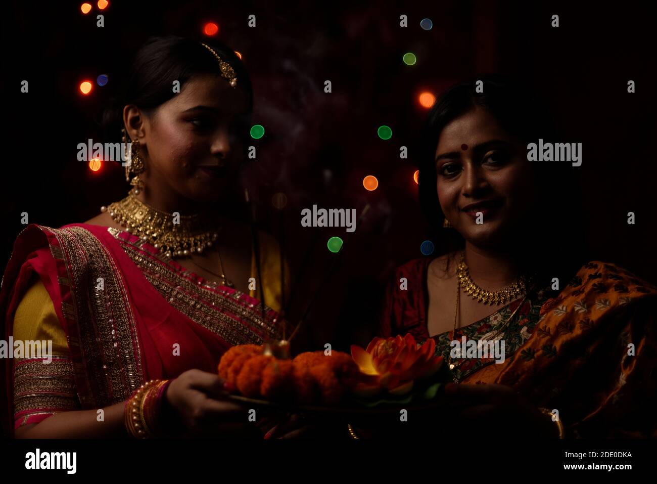 Deux belles femmes bengali indiennes en robe traditionnelle indienne adorant avec des fleurs dans l'obscurité le soir de Diwali. Style de vie indien et Diwali Banque D'Images