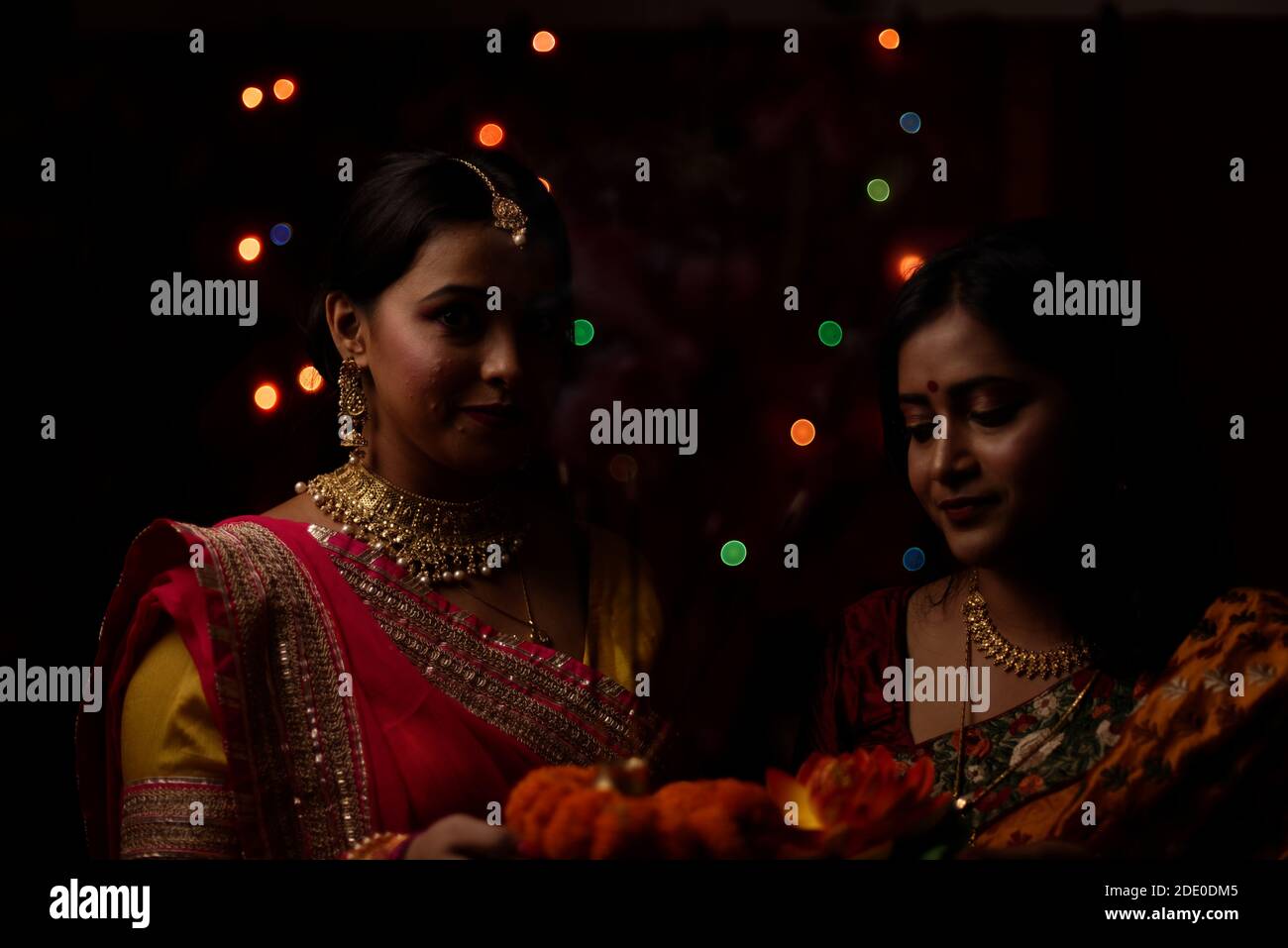Deux belles femmes bengali indiennes en robe traditionnelle indienne adorant avec des fleurs dans l'obscurité le soir de Diwali. Style de vie indien et Diwali Banque D'Images