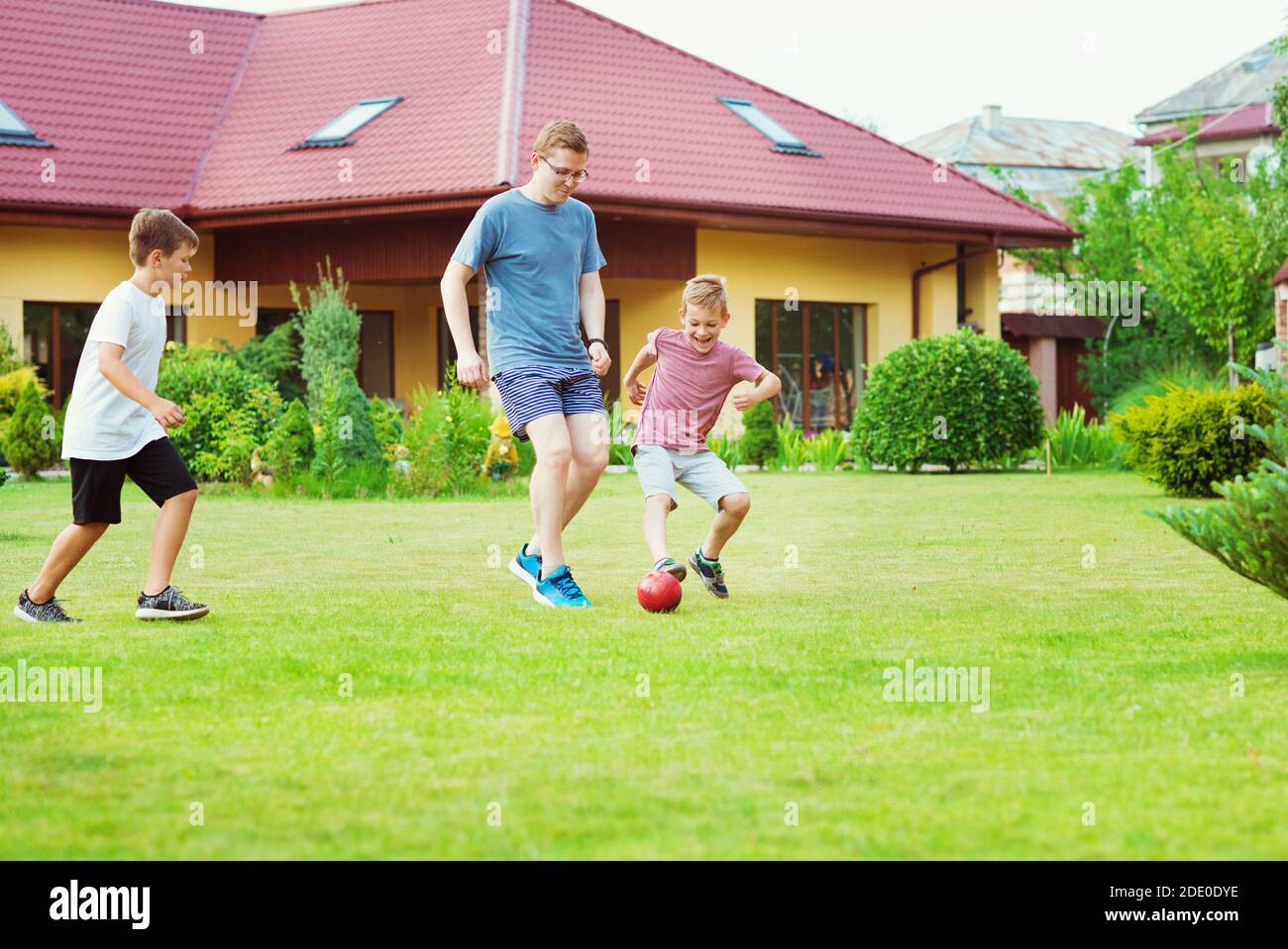 Deux fils heureux jouant au football avec leur père dans le jardin Près de Modern House Banque D'Images