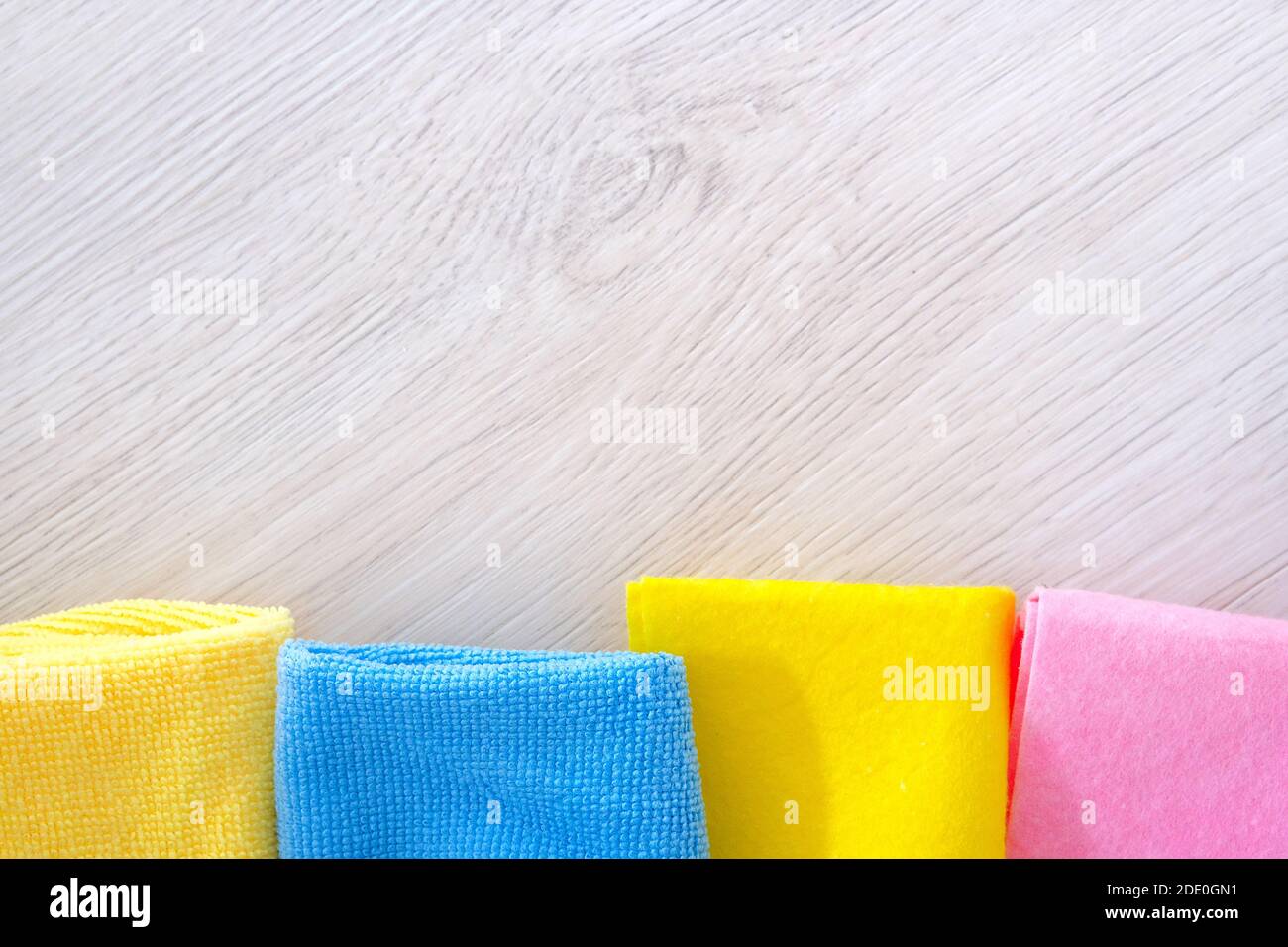 Chiffon en microfibre jaune, bleu et rose sur fond en bois clair avec espace de copie. Vue de dessus. Pose à plat. Les travaux ménagers, le ménage et le concept de ménage. Banque D'Images