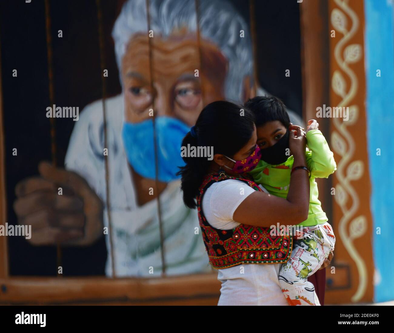 Une femme avec son fils portant un masque facial comme mesure préventive contre le coronavirus marche au-delà d'une murale à Agartala. Tripura, Inde. Banque D'Images