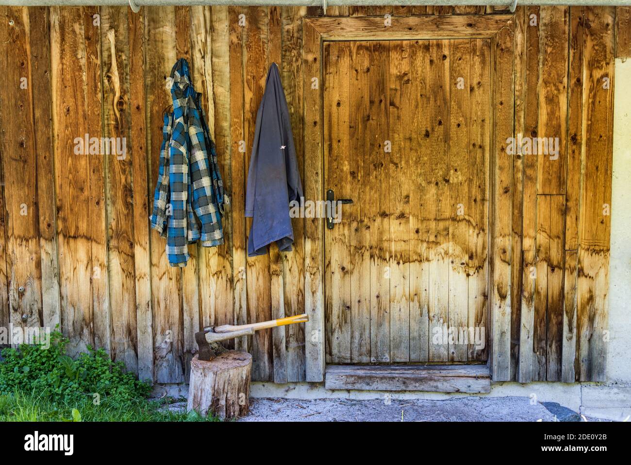 Deux haches en bois coincées dans le coffre à hacher en bois. En arrière-plan, un mur en bois de la maison et deux vêtements de travail accrochés à un crochet. Banque D'Images