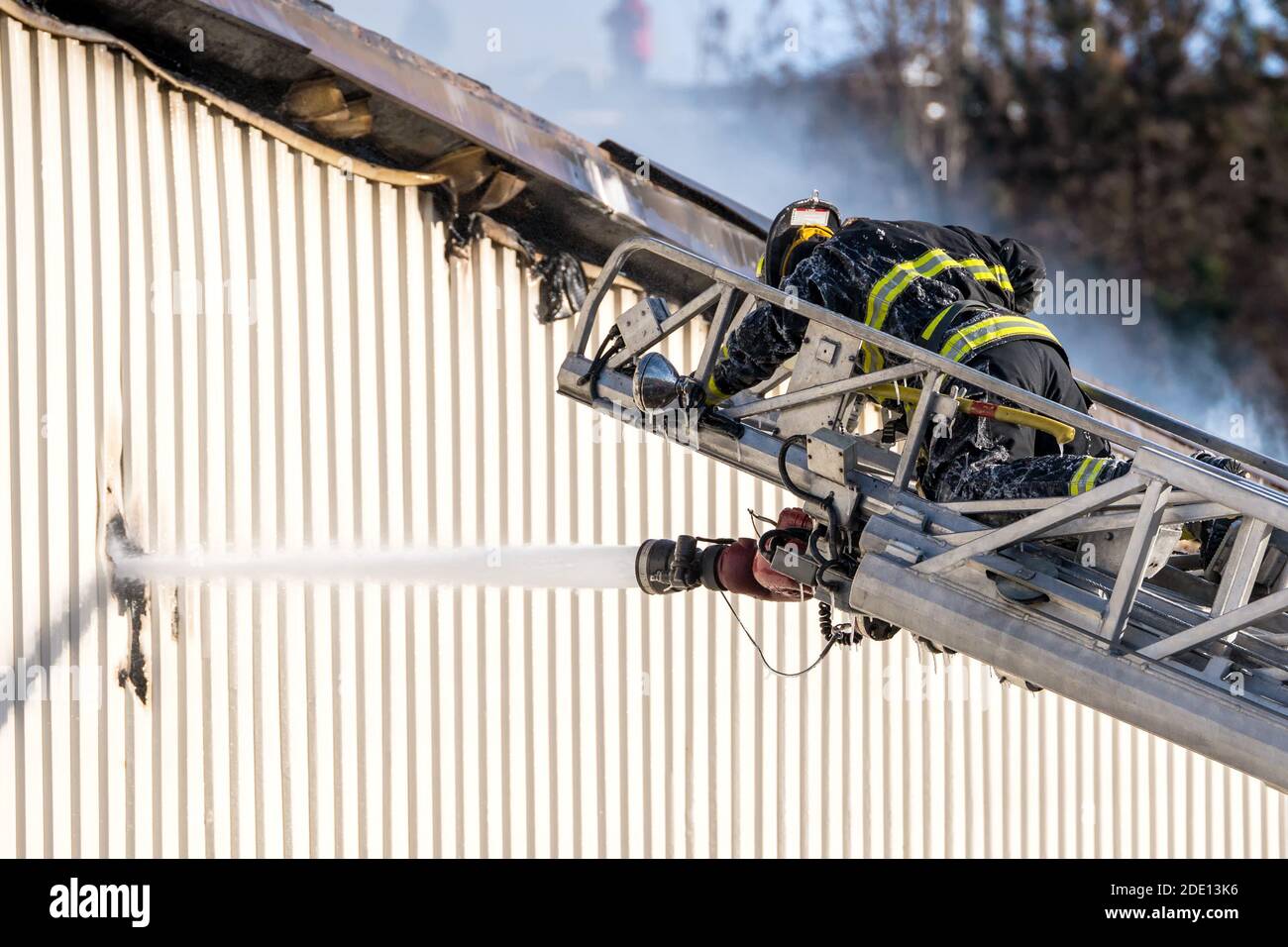 Pompier combattant un incendie de bâtiment au sommet d'une échelle étendue. Un tuyau fixé à l'échelle verse de l'eau dans un trou sur le côté d'un bâtiment. Banque D'Images