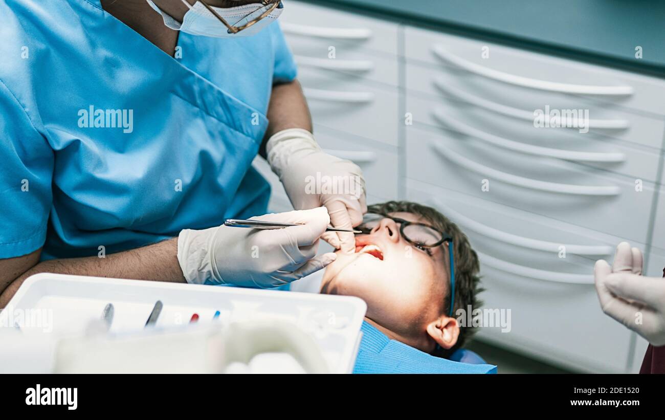 Photo d'un professionnel non reconnu portant un masque facial en raison de l'envid19 faisant un traitement de nettoyage à un jeune garçon. Banque D'Images