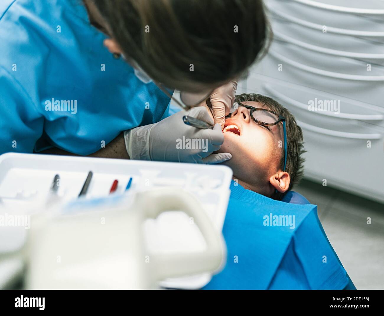 Photo d'un professionnel non reconnu portant un masque facial en raison de l'envid19 faisant un traitement de nettoyage à un jeune garçon. Banque D'Images