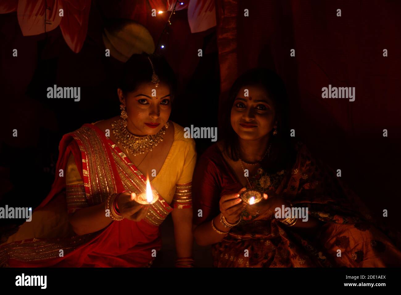 Deux belles femmes bengali indiennes en robe traditionnelle indienne éclairant les lampes Diwali assis sur le sol le soir de Diwali. Style de vie indien Banque D'Images