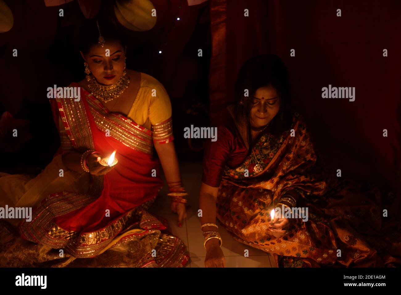 Deux belles femmes bengali indiennes en robe traditionnelle indienne éclairant les lampes Diwali assis sur le sol le soir de Diwali. Style de vie indien Banque D'Images