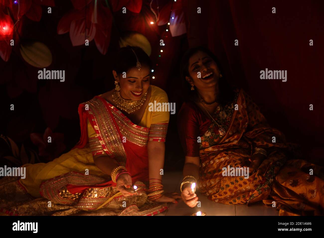 Deux belles femmes bengali indiennes en robe traditionnelle indienne éclairant les lampes Diwali assis sur le sol le soir de Diwali. Style de vie indien Banque D'Images