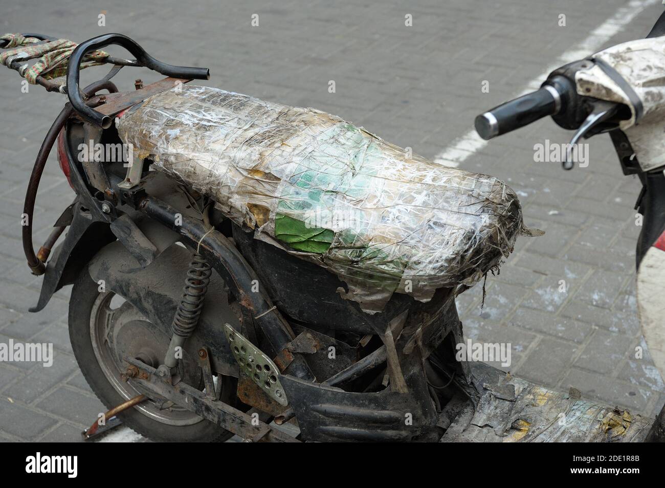 Vieux et réparé avec du ruban adhésif scooter garé dans la rue. garé contre mur vieilli. Banque D'Images