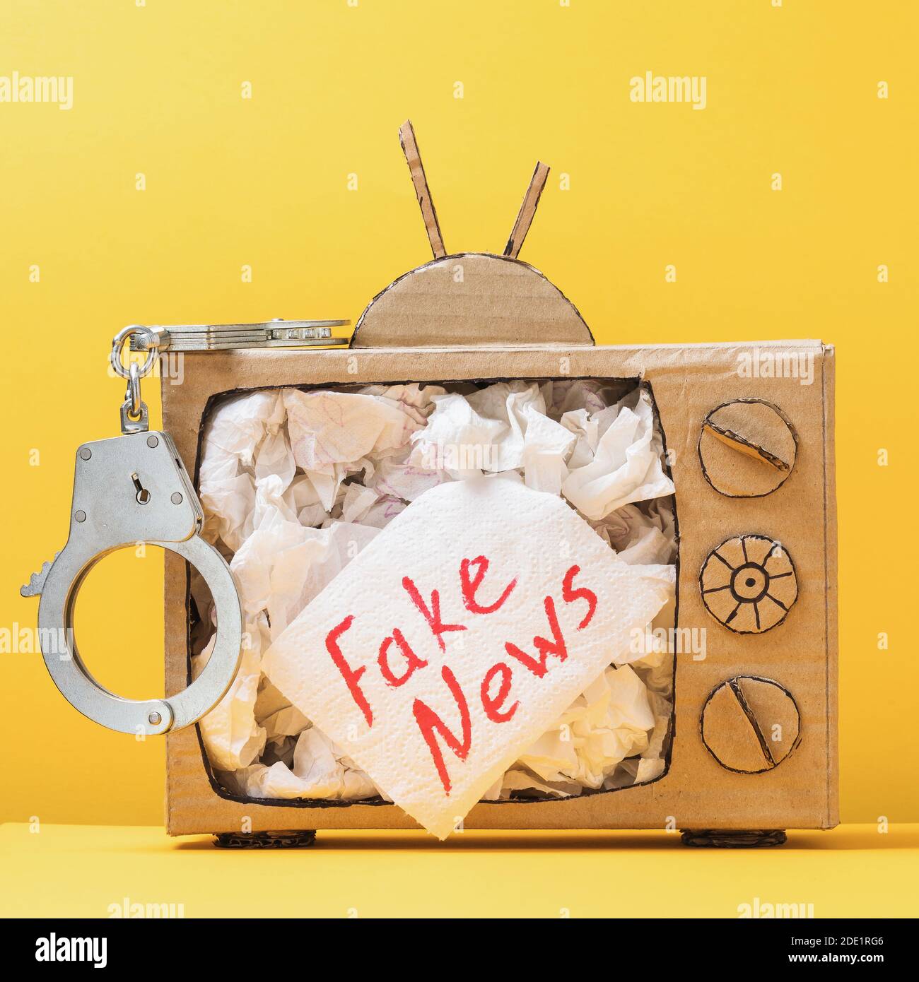 Modèle de téléviseur en carton avec menottes et papier toilette sortant de l'écran avec une inscription. Concept de punition pour les fausses nouvelles. Banque D'Images