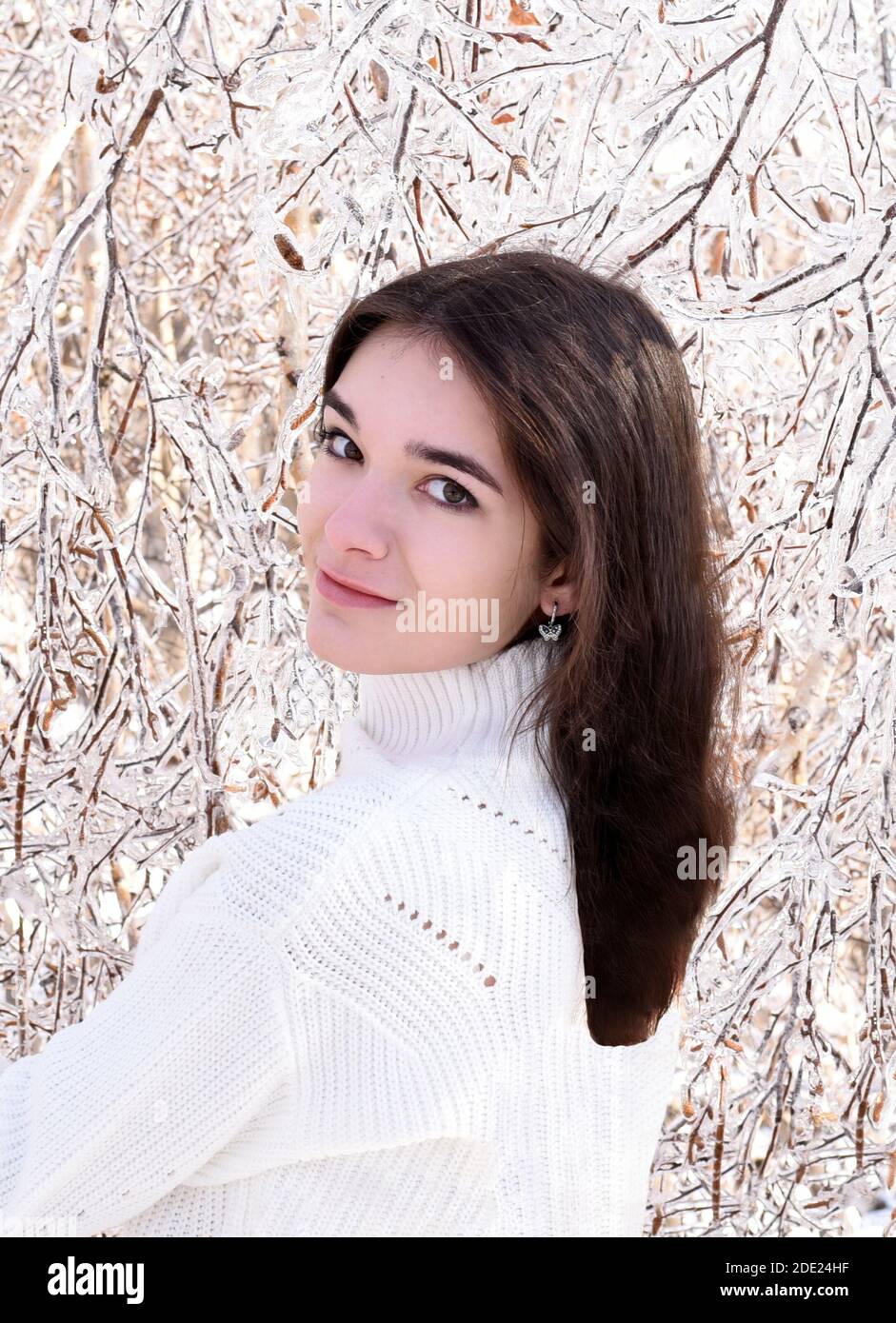 Portrait d'une jeune femme russe en chandail blanc regardant la caméra à côté des branches gelées de bouleaux, couvertes de glace. Forêt d'hiver en Russie Banque D'Images