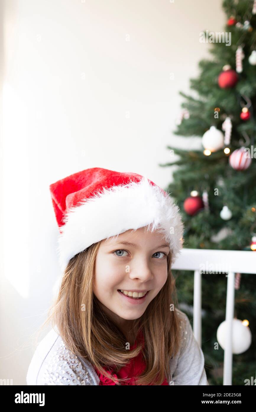 Jolie fille dans santa clause chapeau devant un Arbre de Noël en appréciant Noël Banque D'Images