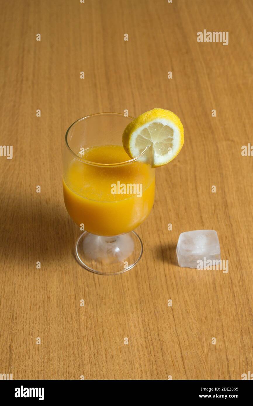 Délicieux jus d'orange et de pomme dans un élégant verre avec un cube de glace sur la table en bois dans une cuisine rustique. Banque D'Images